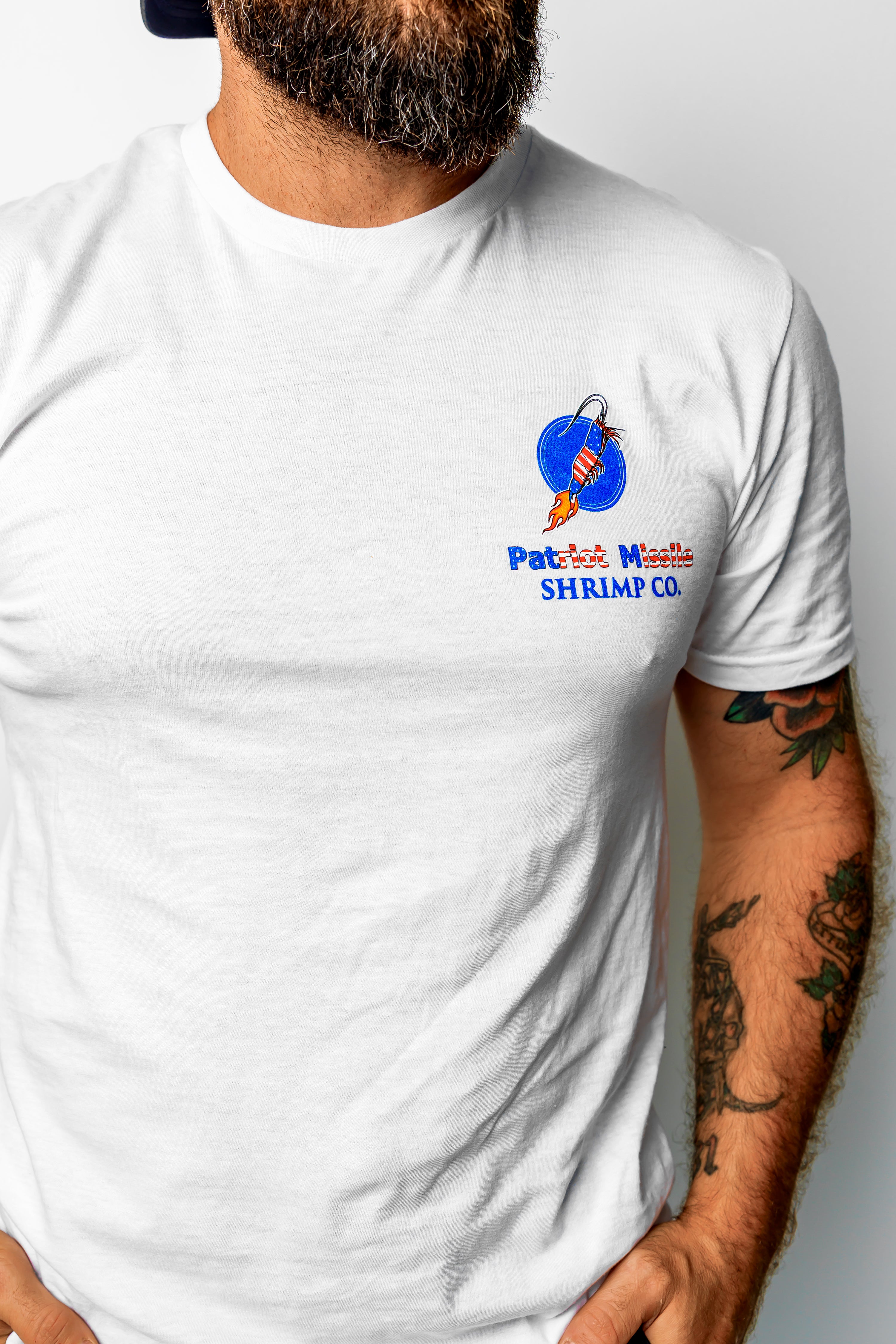 A man wearing a white crewneck t-shirt with a colorful 'Patrick's Whisht Shrimp Co.' logo printed on the left chest.